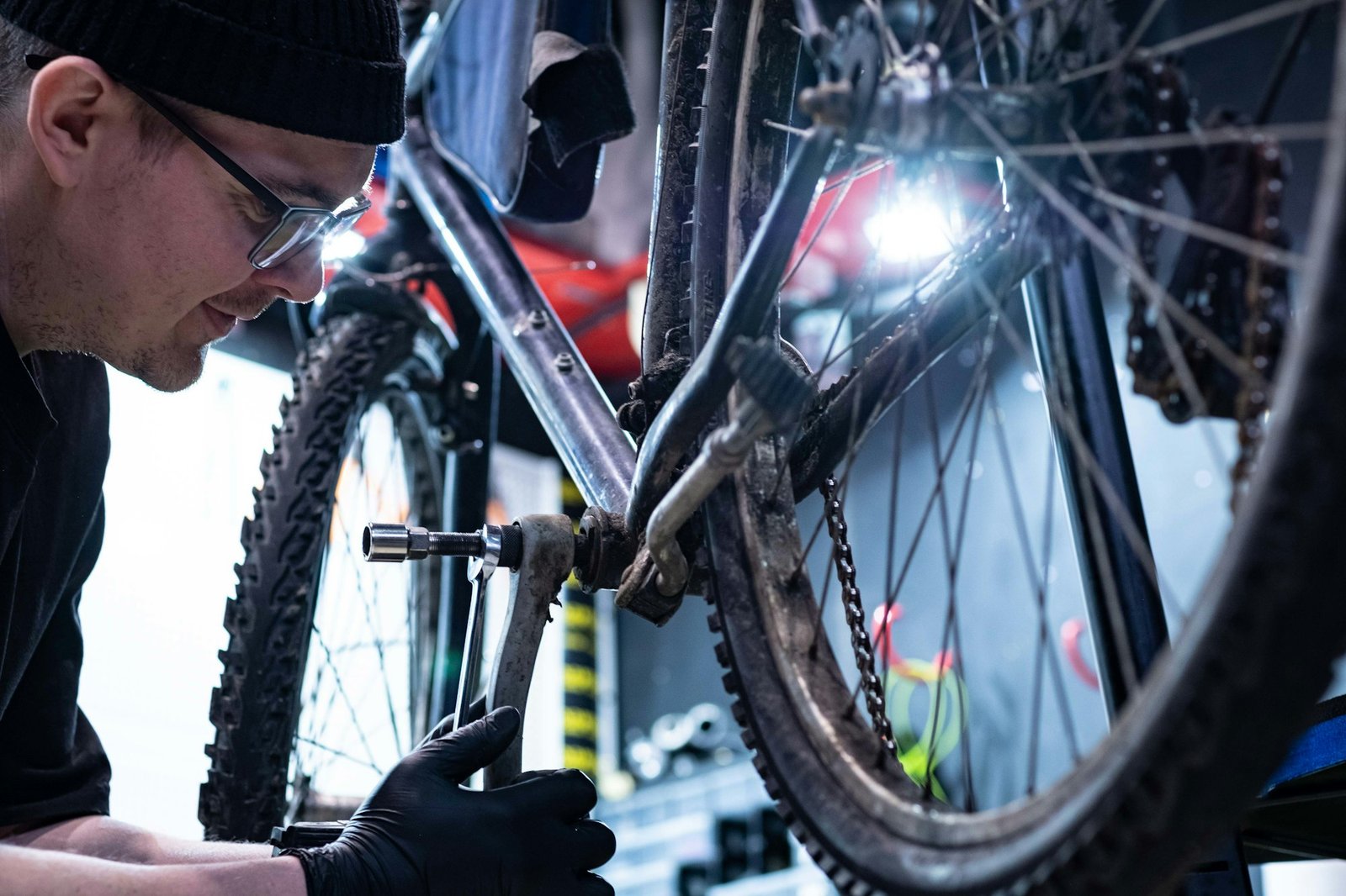 Mecánico con lentes y gorro ajustando el pedal de una bicicleta de montaña en el taller